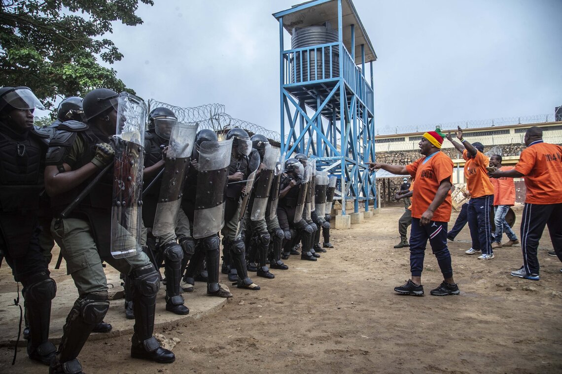 A training exercise is conducted in the Ngaragba Central Prison in Bangui to build the capacity of prison officers to manage a riot by inmates, supported by the UN peacekeeping mission MINUSCA. Photo: Hervé Serefio / MINUSCA. A group of riot police officers holding shields standing in a line with men facing men in orange shirts