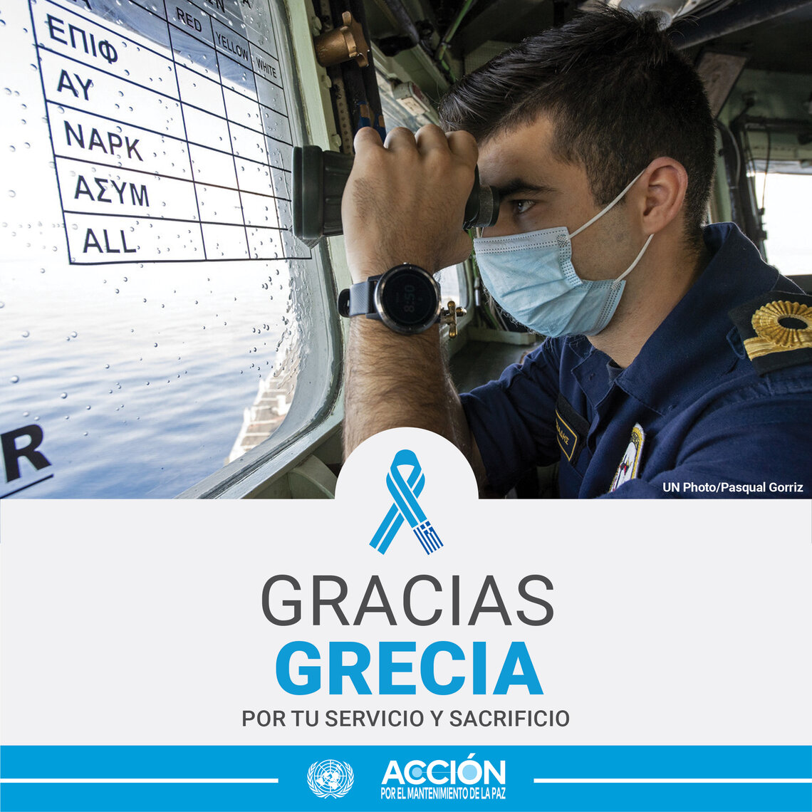 Un casco azul griego, con mascarilla, mirando con unos prismaticos desde el interior de un barco. 