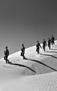 Peacekeepers walking in single file down a sand dune.