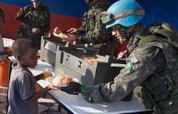 A peacekeeper serving food to a young boy.