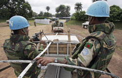 Two peacekeepers riding on the top of a truck driving down a dirt road.
