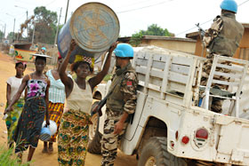 Women walking by UNOCI Peacekeepers, one woman carrying an empty barrel on her head.