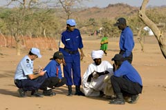 UN Police officers standing and squating around a man in a desert landscape with brush in the background.