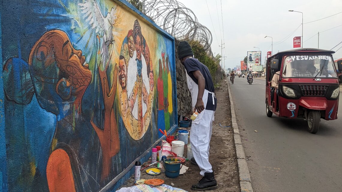 Photo of street artist Didier Binyungu creating a mural in North Kivu.