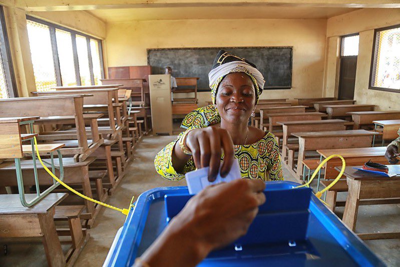 A woman casts her vote in an empty room with desks and a blackboard