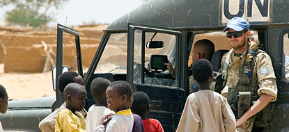 A peacekeeper and children in front of a UN vehichle.