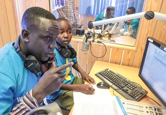 Two young people wearing headphones sitting in front of a radio microphone.