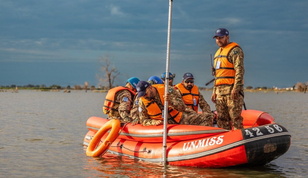 UNMISS engineers in a small boat measure flood levels with a large ruler