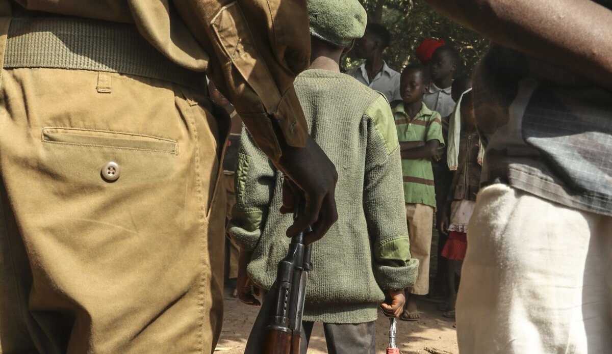 a child stands at attention wearing a uniform and carrying a gun