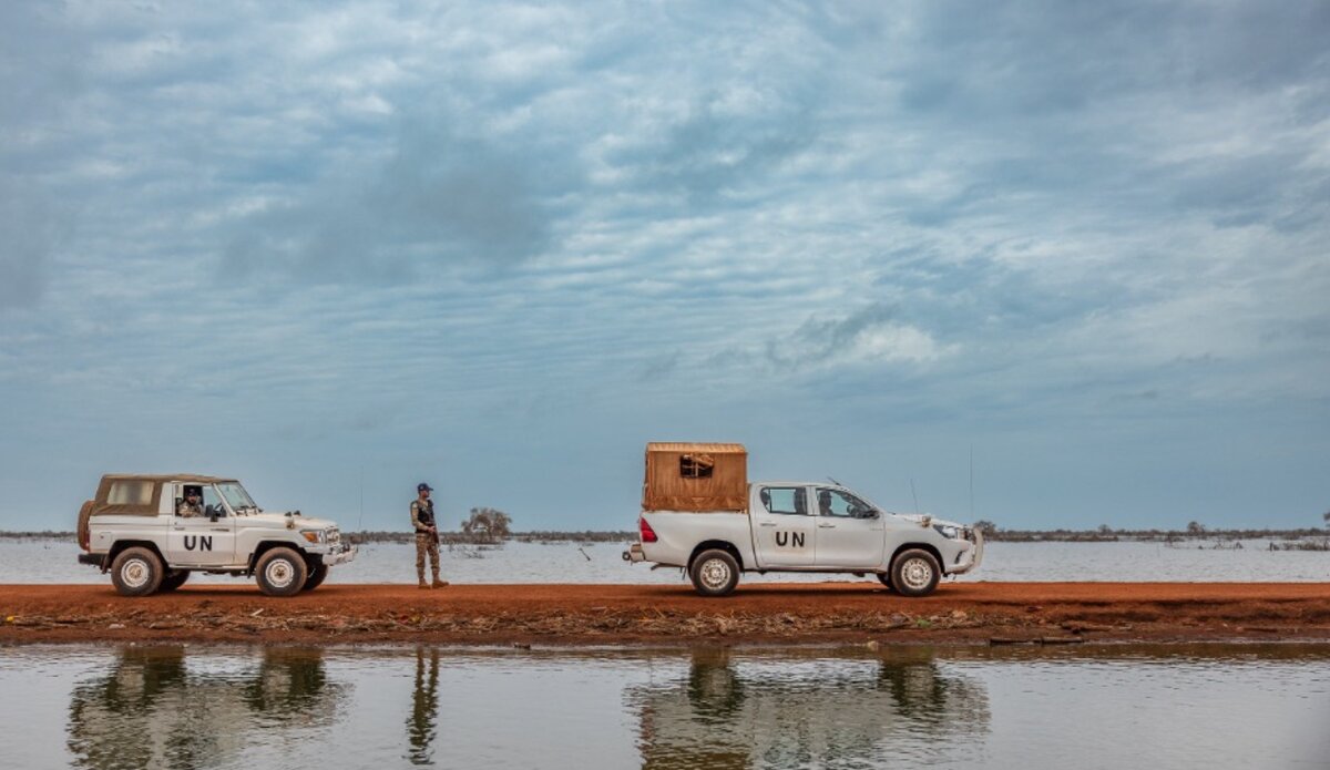 UN vehicles navigate a road surrounded by water