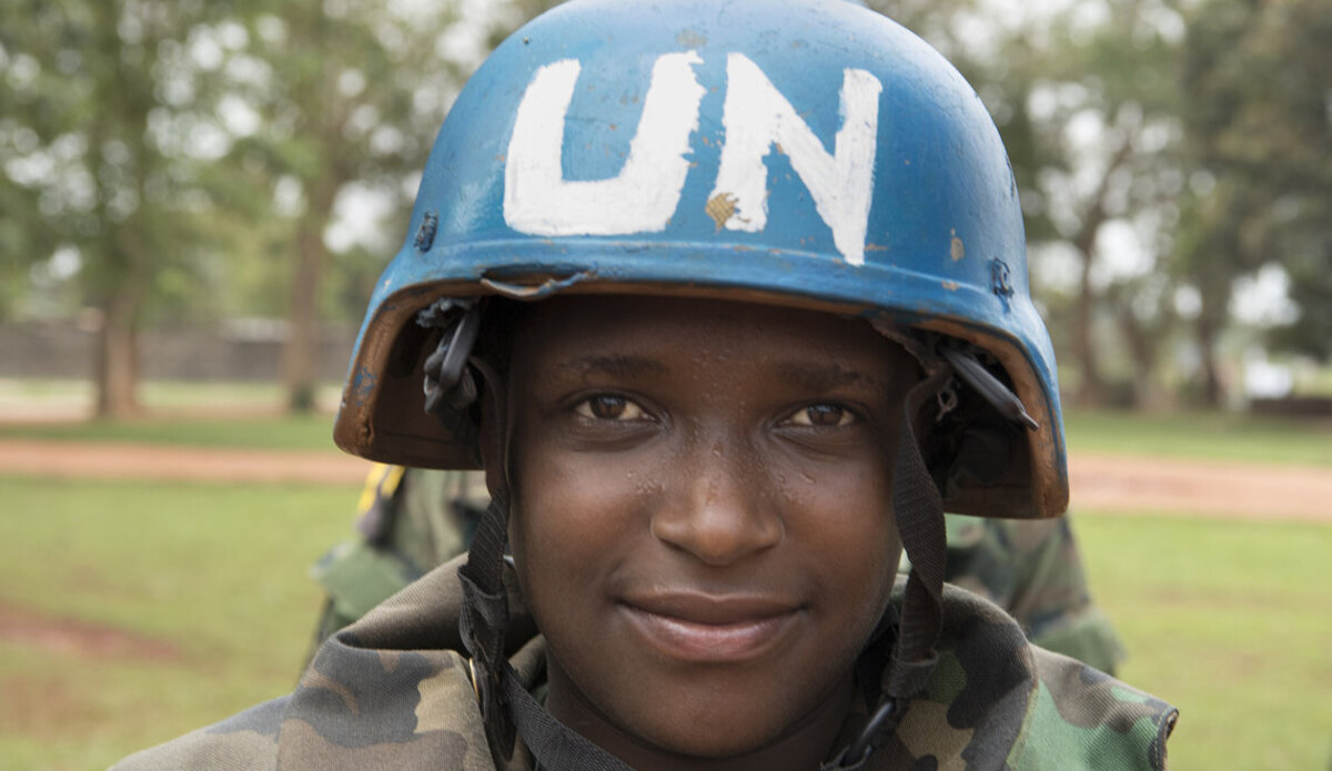 A UN peacekeeper in a blue UN helmet smiles at the camera