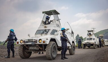 UN soldiers stand next to armoured vehicles on a dusty road