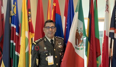 Major General Ramón Guardado Sánchez standing in front of a row of flags holding the Mexican Flag