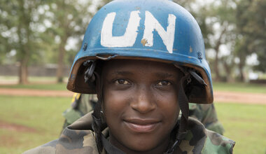 A UN peacekeeper in a blue UN helmet smiles at the camera