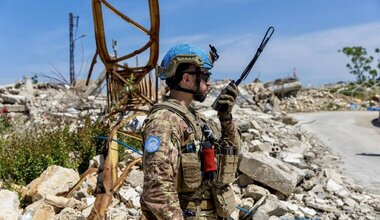 A UN peacekeeper in military uniform stands amid rubble