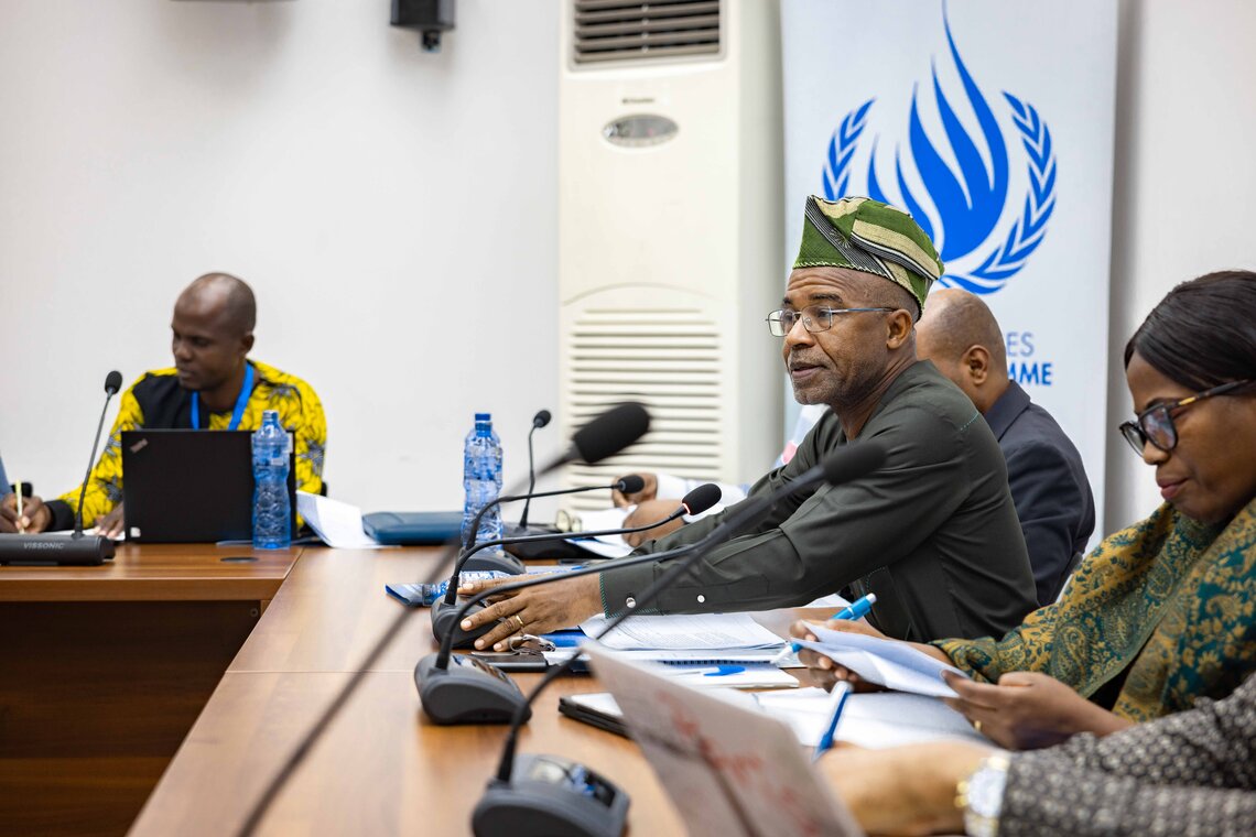 Men and women sit at a conference table in front of microphones