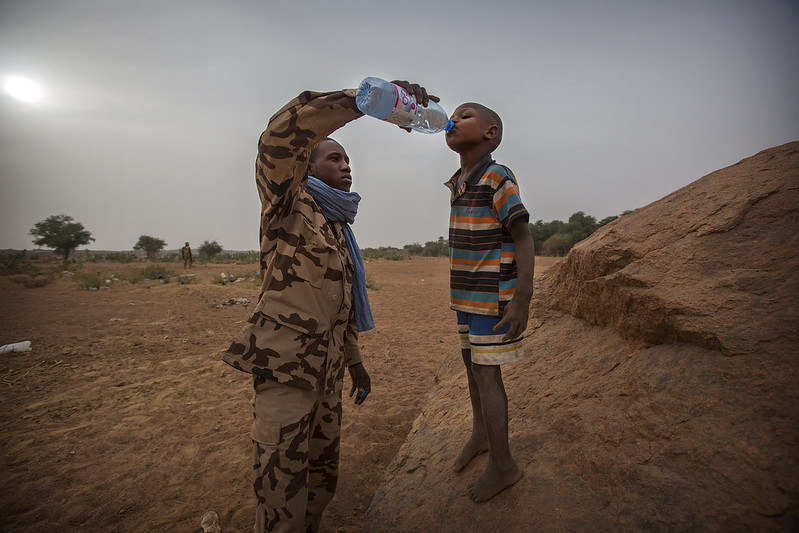 A member of the Chadian contingent of the United Nations Multidimensional Integrated Stabilization Mission in Mali (MINUSMA) offers a boy a drink of water. Photo credit: UN Photo/Sylvain Liechti